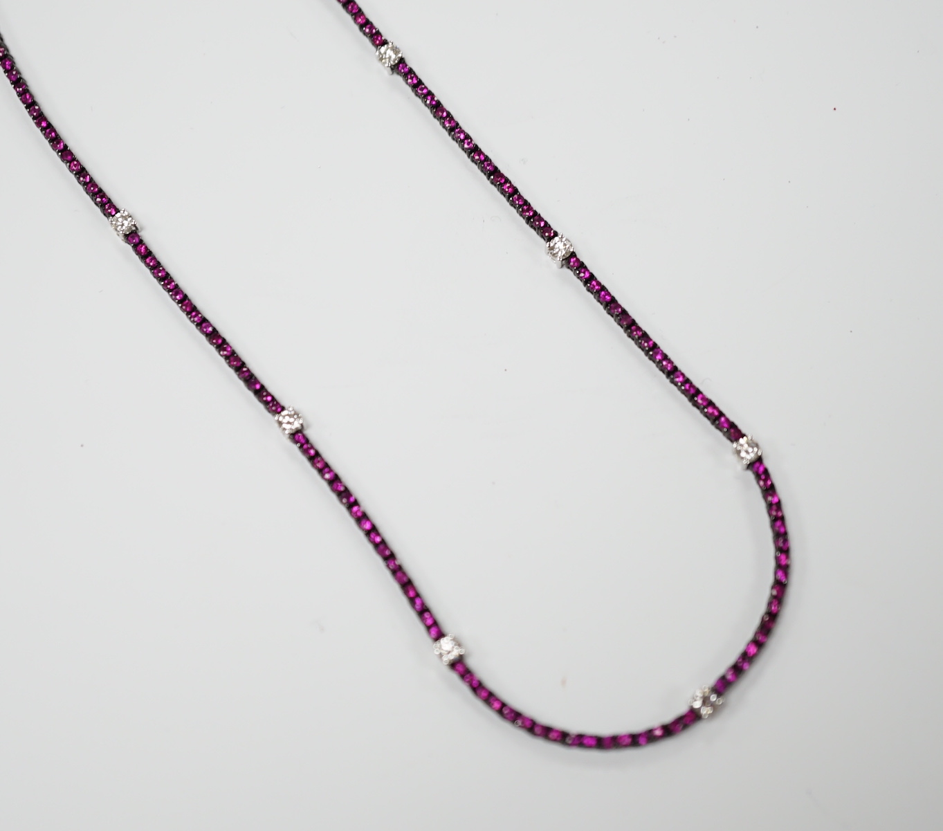 A modern blackened 18k, ruby and diamond line cluster set necklace, 42cm, gross weight 10.3 grams.